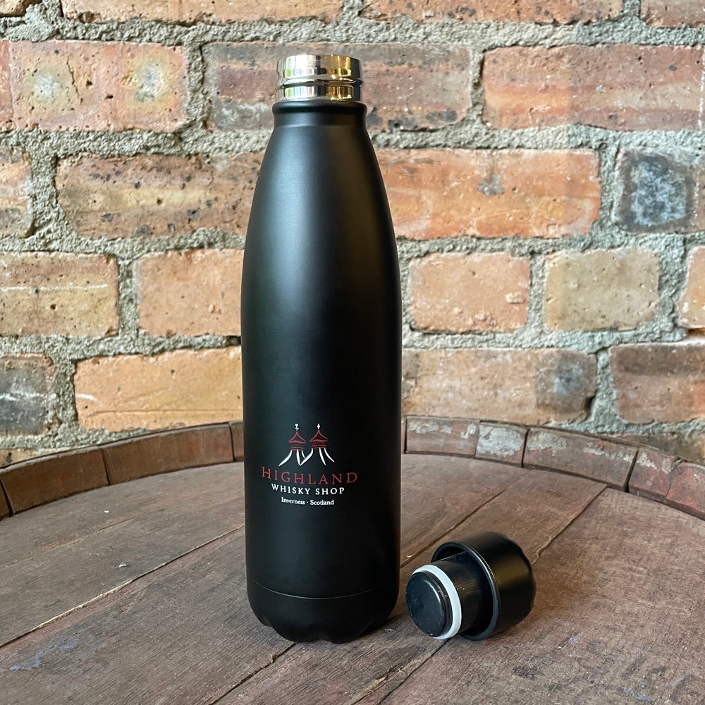 Black insulated bottle with 'Highland Whisky Shop' logo on a wooden surface with a brick wall background