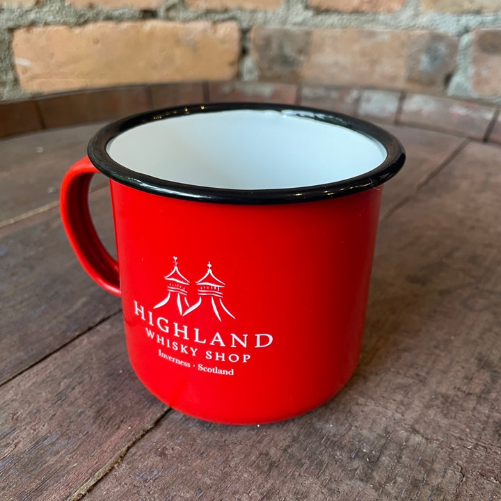 Red enamel mug with 'Highland Whisky Shop' logo on a wooden surface with a brick wall background