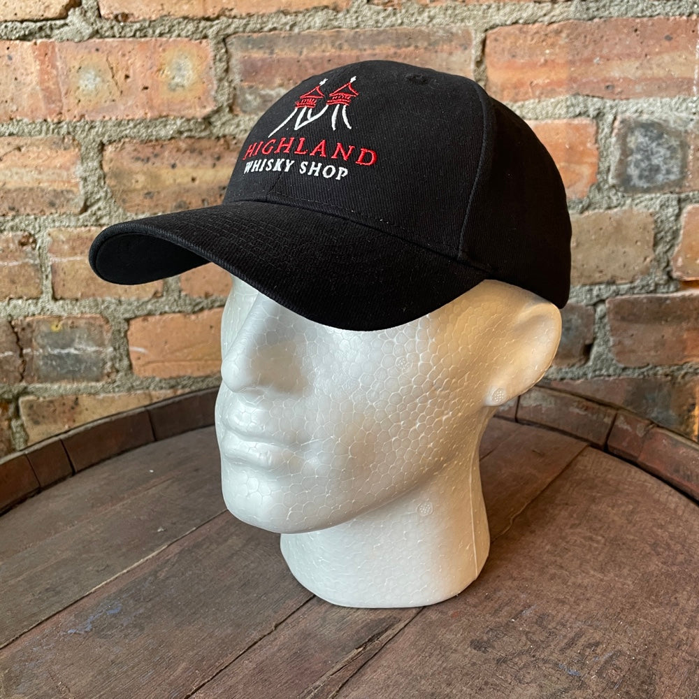 Black cap with 'Highland Whisky Shop' text on a mannequin head against a brick wall.