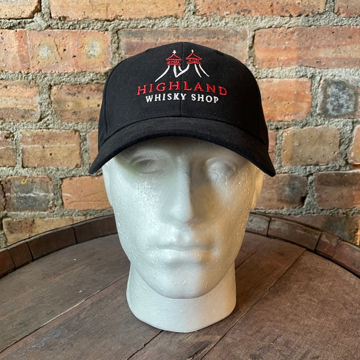 Black cap with 'Highland Whisky Shop' text and logo on a mannequin head against a brick wall.