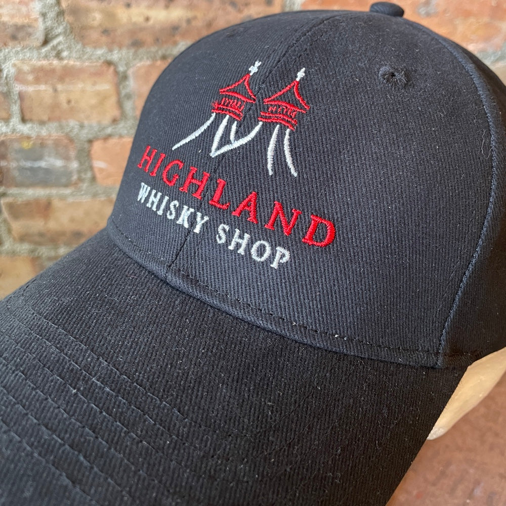 Black cap with 'Highland Whisky Shop' embroidery against a brick wall background